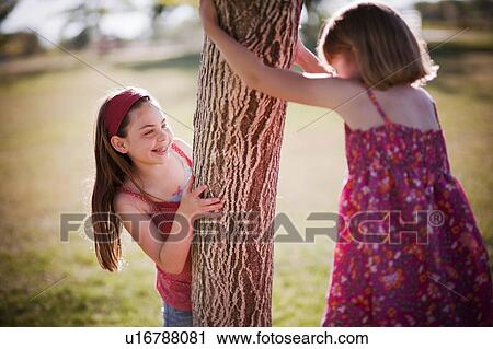 Stock Image - 2 young girls playing around tree. Fotosearch