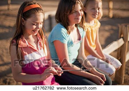 Stock Image - 3 young girls sitting on fence. Fotosearch