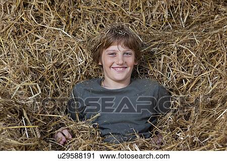 Stock Image - Boy in hay, smiling. Fotosearch