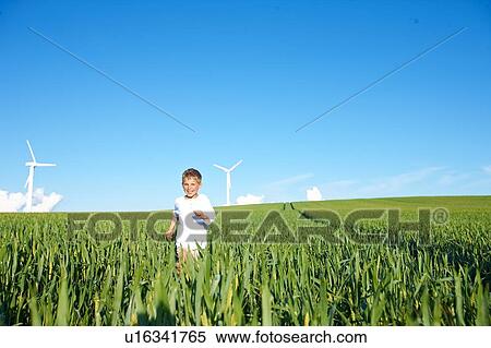 Stock Photography - Boy running on field with wind turbines. Fotosearch