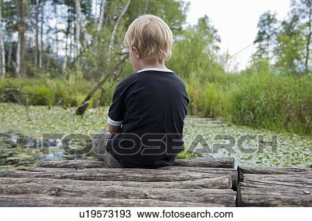 Stock Image - Boy sitting on a landing stage. Fotosearch