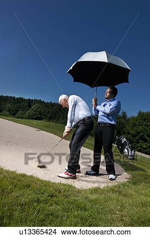 Caddy is holding a parasol over a golfer View Large Photo Image Picture - Caddy is holding a parasol over a golfer. Fotosearch