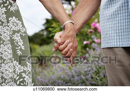 Stock Image - Close-up of mature couple holding hands. Fotosearch