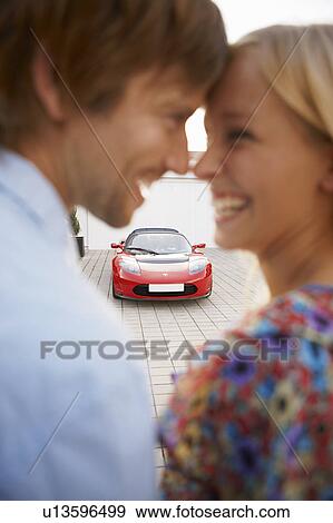 Stock Photo - Couple close, electric car in background. Fotosearch