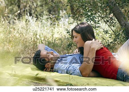 Stock Image - Couple cuddling on picnic blanket. Fotosearch