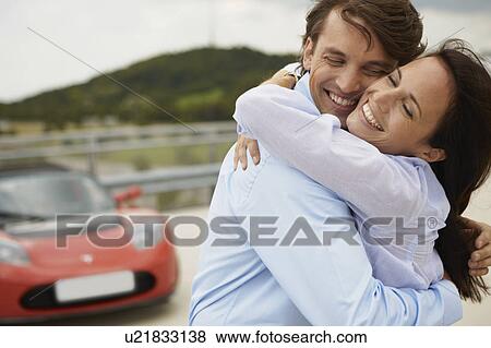 Stock Photo - Couple hugging in front of electric car. Fotosearch