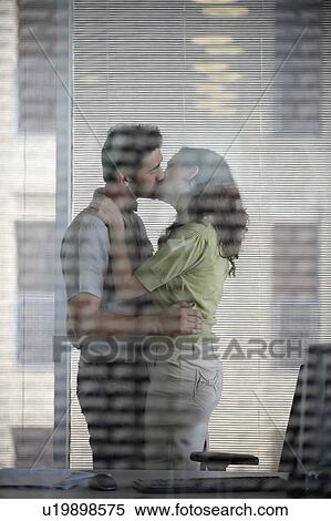 Stock Photography - Couple kissing in office. Fotosearch