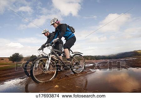 Picture - Couple mountain biking in countryside. Fotosearch