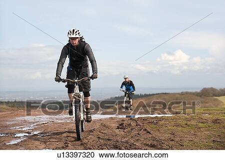 Stock Image - Couple mountain biking in countryside. Fotosearch