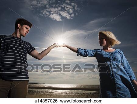 Stock Photograph - Couple on beach holding sun in hands. Fotosearch