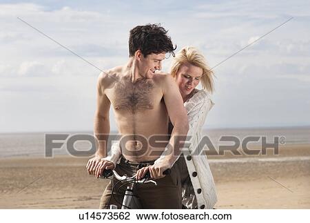 Stock Image - Couple on beach on bike. Fotosearch