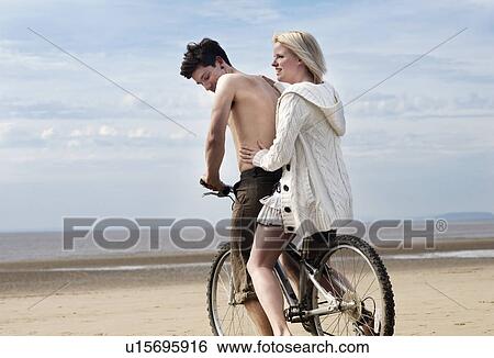 Stock Photograph - Couple on bike on beach. Fotosearch
