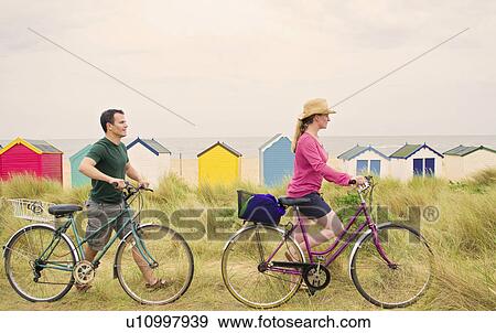 Stock Photo - Couple push bicycles over beach. Fotosearch
