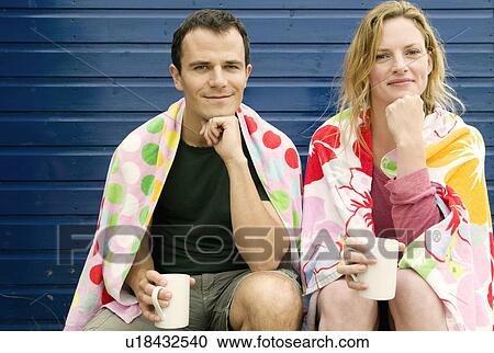 Stock Image - Couple relax with hot drinks on beach. Fotosearch