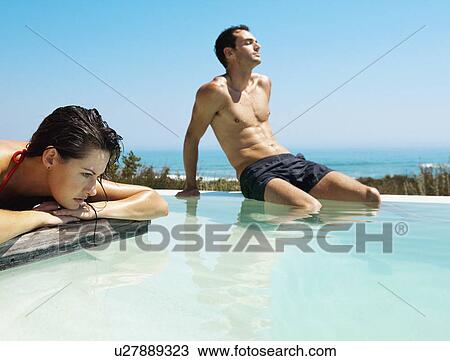 Stock Image - Couple relaxing by infinity pool. Fotosearch