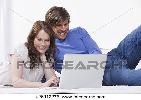 Couple relaxing on rug using a laptop View Large Photo Image Stock Photograph - Couple relaxing on rug using a laptop. Fotosearch