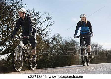 Stock Photograph - Couple riding bikes on countryside road. Fotosearch