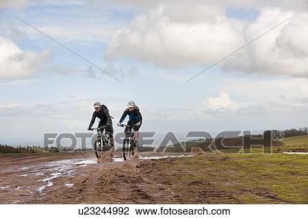 Couple riding mountain bikes through mud View Large Photo Image Stock Image - Couple riding mountain bikes through mud. Fotosearch
