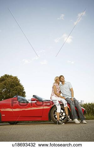 Stock Image - Couple sitting on electric sports car. Fotosearch