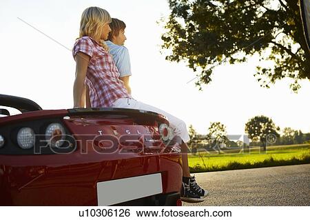 Stock Photograph - Couple sitting on their electric car. Fotosearch