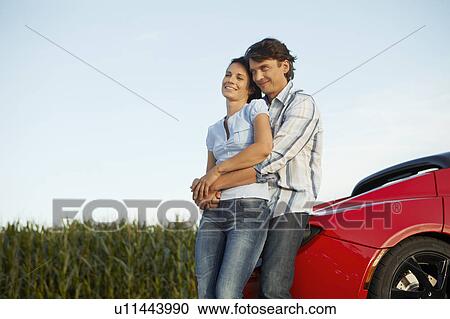 Stock Image - Couple standing by their electric car. Fotosearch