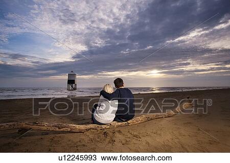 Stock Image - Couple watching sunset on beach. Fotosearch