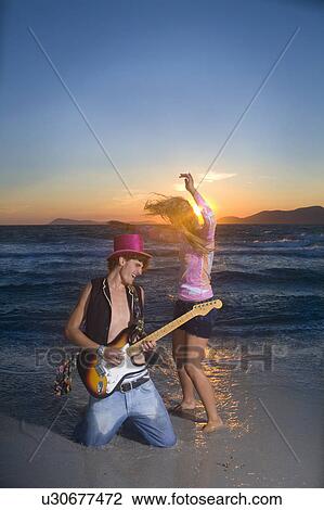 Stock Image - Cple play guitar and dance at sunset sea. Fotosearch