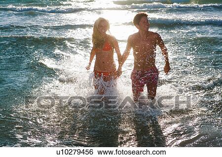 Stock Photograph - Cple run at sea hold hands in sunset. Fotosearch