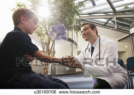 Stock Photograph - Doctor greeting young boy in surgery. Fotosearch