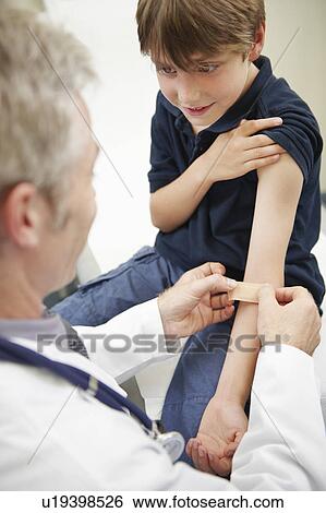 Doctor putting plaster on young boy View Large Photo Image Stock Photograph - Doctor putting plaster on young boy. Fotosearch