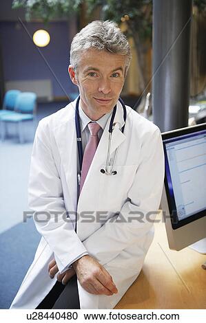 Doctor siting on desk in surgery View Large Photo Image Stock Image - Doctor siting on desk in surgery. Fotosearch