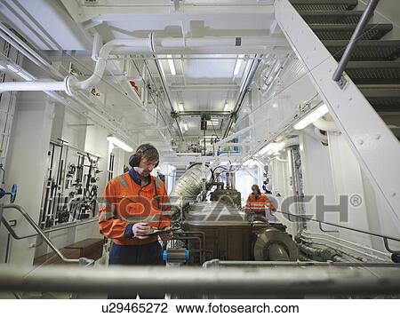 Stock Image - Engineers in ship's engine room. Fotosearch