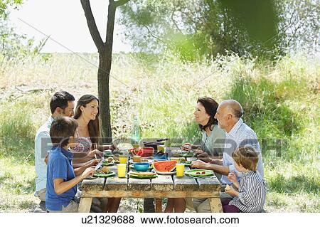 Stock Photo - Family eating meal on outdoor table. Fotosearch