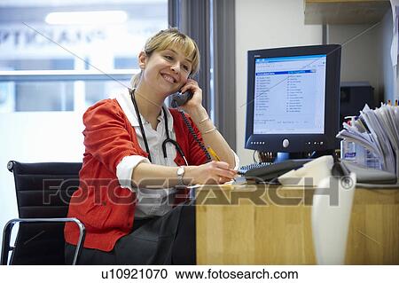 Stock Image - Female doctor on telephone in office. Fotosearch