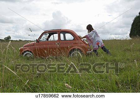 Stock Image - Female pushing car in field. Fotosearch