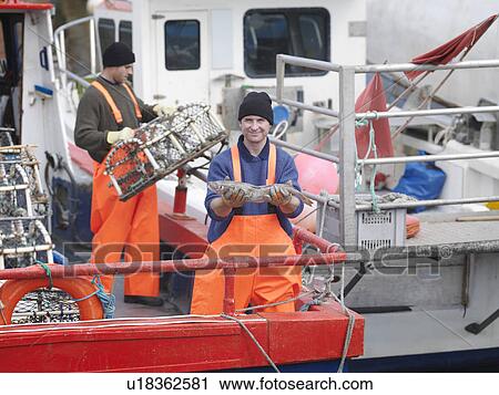 Stock Image - Fisherman holds fish on boat in harbour. Fotosearch