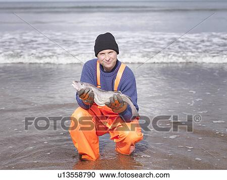 Fisherman on shore holding fish View Large Photo Image Stock Image - Fisherman on shore holding fish. Fotosearch