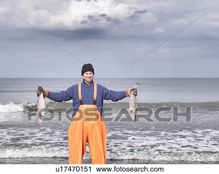 Stock Image - Fisherman on shore holding fish. Fotosearch