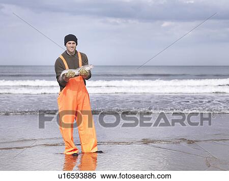 Fisherman on shore holding fish View Large Photo Image Stock Photograph - Fisherman on shore holding fish. Fotosearch