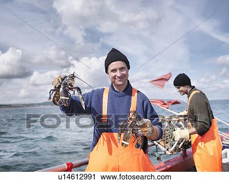 Stock Image - Fishermen on boat holding lobsters. Fotosearch