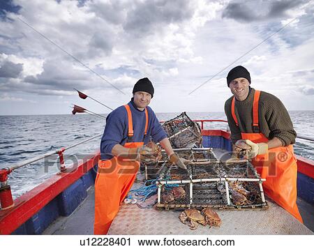 Stock Image - Fishermen sort catch of crabs on boat. Fotosearch