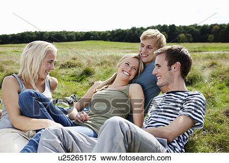 Stock Photography - Four young persons sitting in grass. Fotosearch