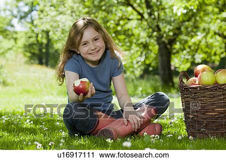 Stock Image - Girl in meadow, eating apple. Fotosearch