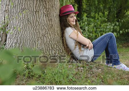 Girl in pink hat sitting against tree View Large Photo Image Stock Image - Girl in pink hat sitting against tree. Fotosearch