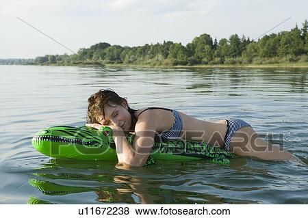 Stock Photo - Girl laying on air crocodile in water. Fotosearch