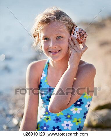 Stock Photo - Girl listening to shell at the beach. Fotosearch