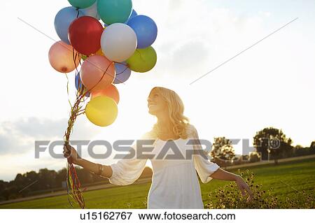 Stock Photo - Girl with balloons outside at sunset. Fotosearch