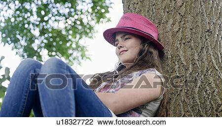 Girl with headphones leaning on tree View Large Photo Image Stock Image - Girl with headphones leaning on tree. Fotosearch