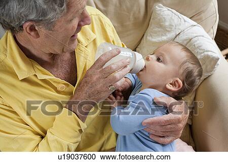 Stock Image - Grandad feeding grandson milk bottle. Fotosearch