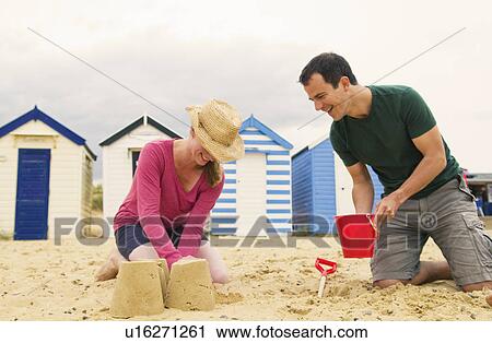 Stock Image - Happy couple make sandcastles on beach. Fotosearch